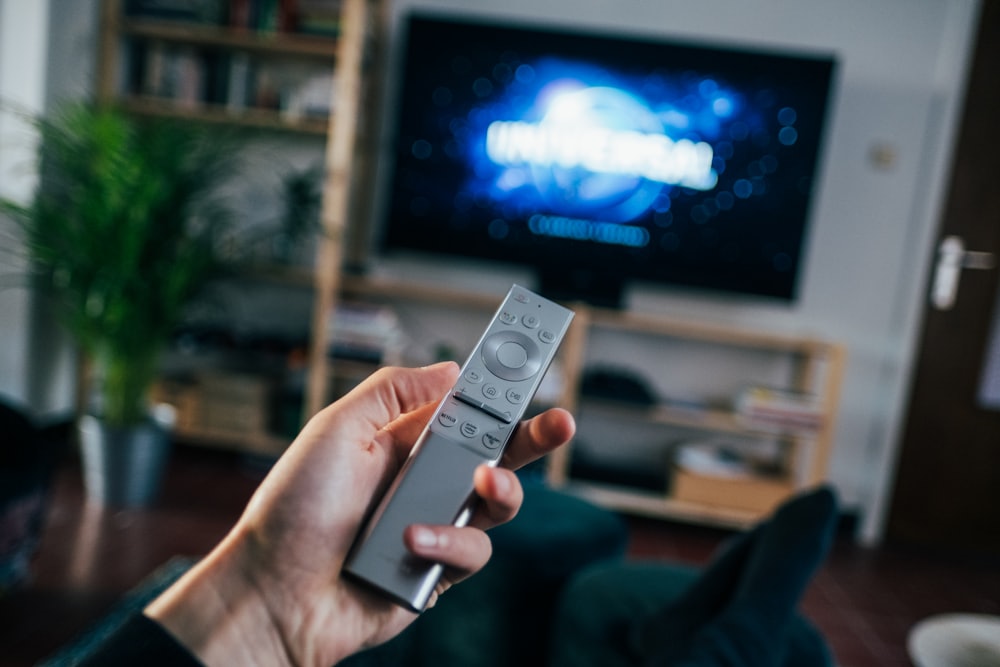 Person holding a television remote control in front of a screen